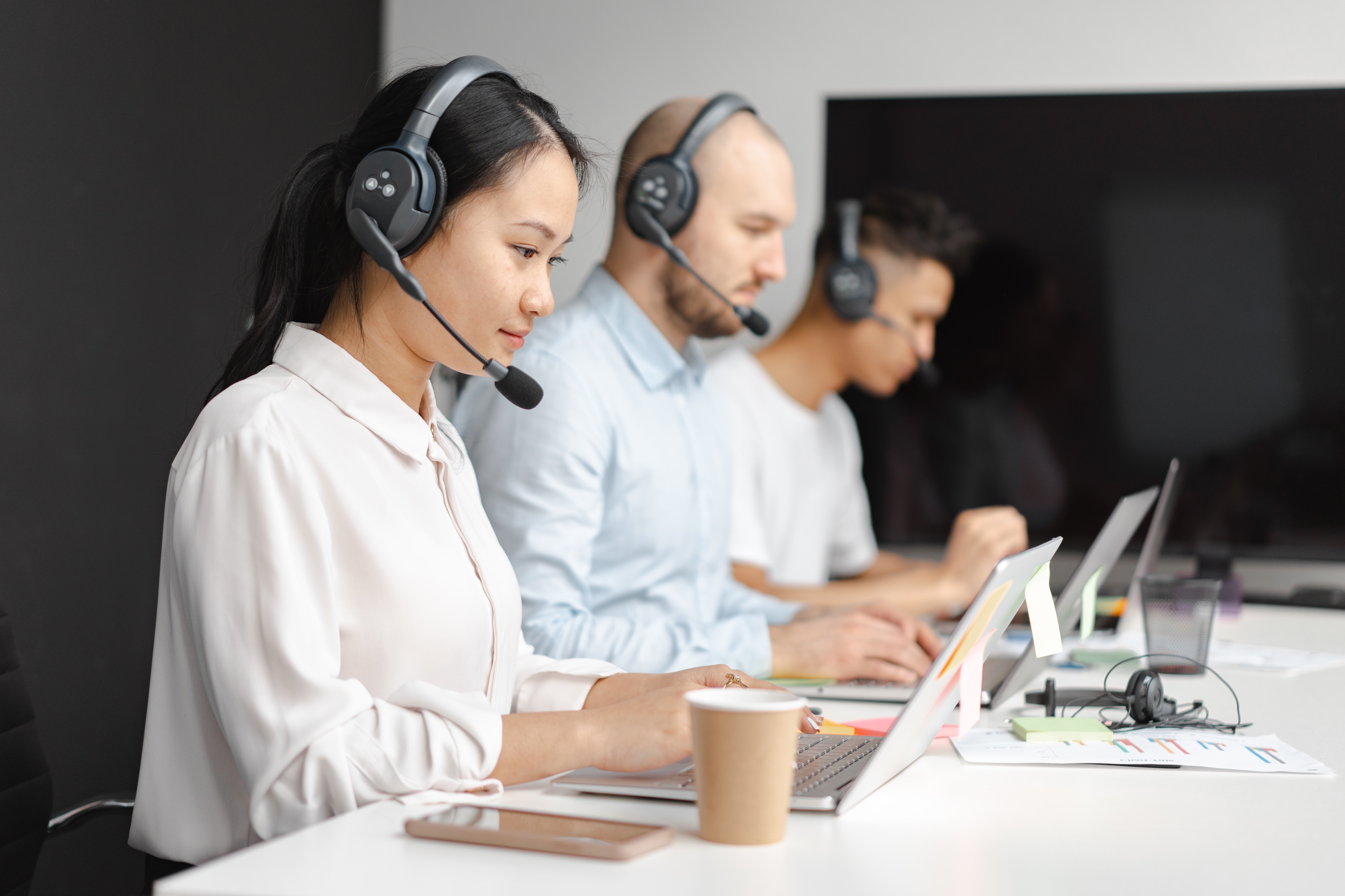 A photo capturing 3 callers with headphones on, connected to a mic, as they type on their laptops 