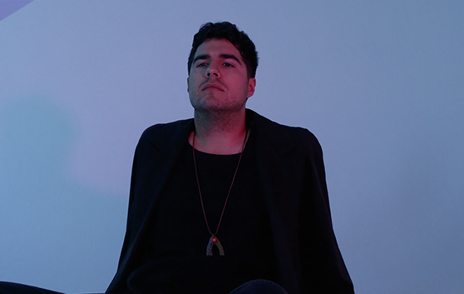 A picture of Jeremy Dutcher standing in front of a blue wall
