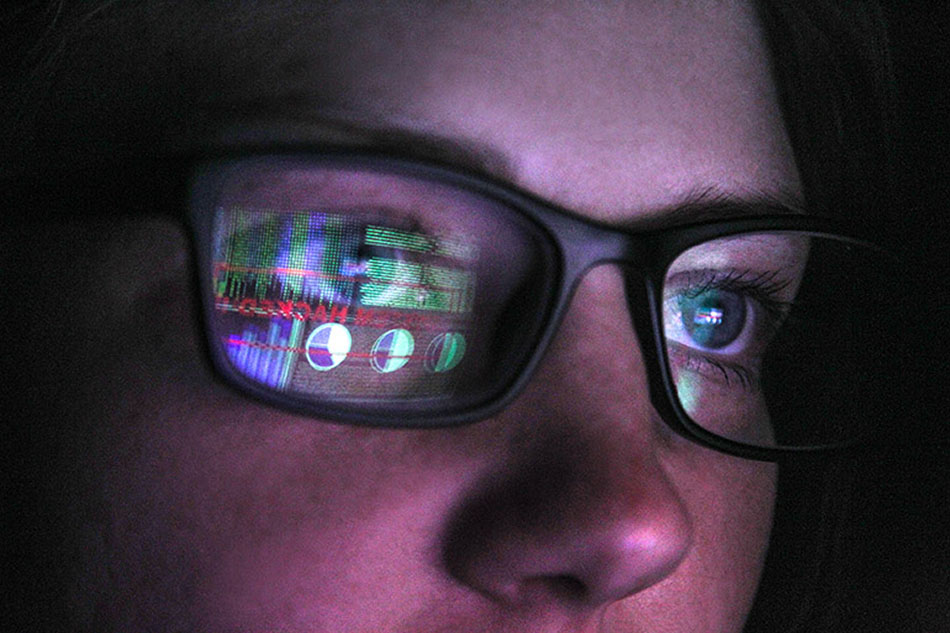 A close up of a woman wearing glasses with a screen reflected on the glasses