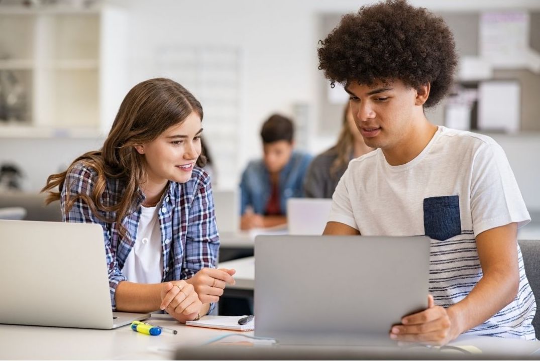 Two secondary school students working together on laptops.