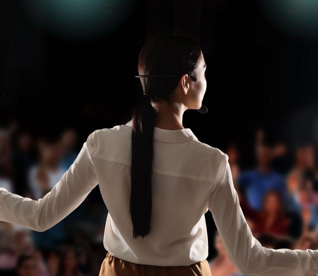 Image of a speaker on a platform, presenting to the audience, at a Symposium event.