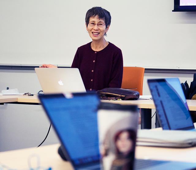 A picture of Professor Ryuko Kubota in class, laughing, sitting in front of a laptop computer