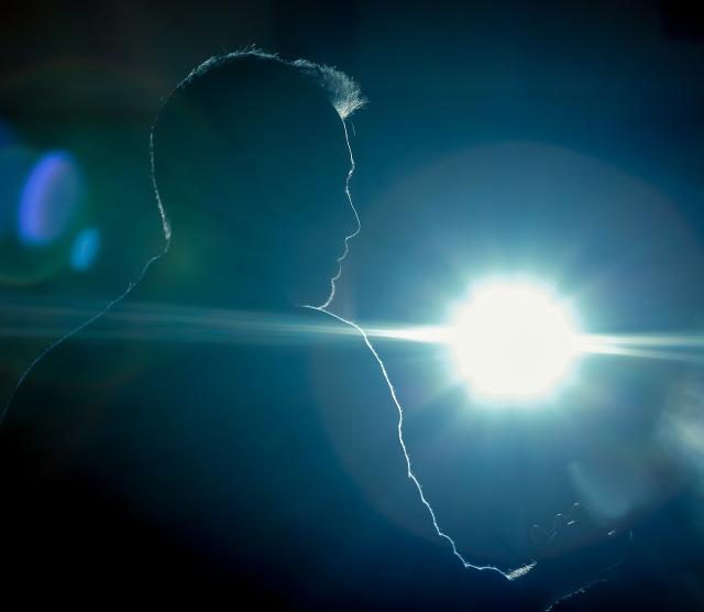A photo of a mans silhouette, holding a phone, lit up by a spotlight