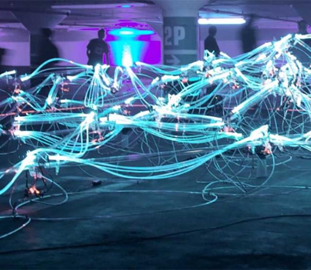 An image of lit up wires criss crossing, with people standing in the background