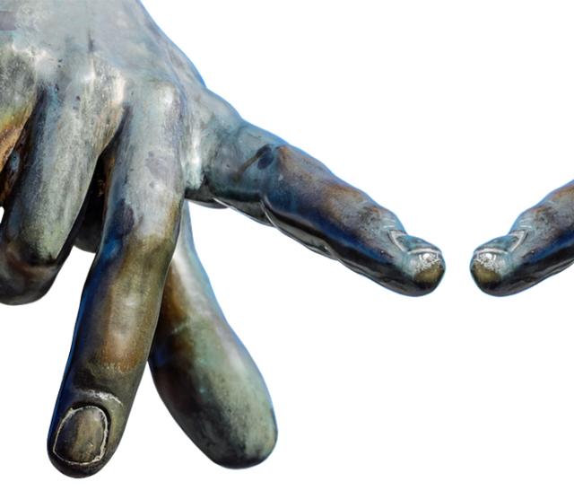A picture of part of a brass statues hands, reaching out with index fingers almost touching.