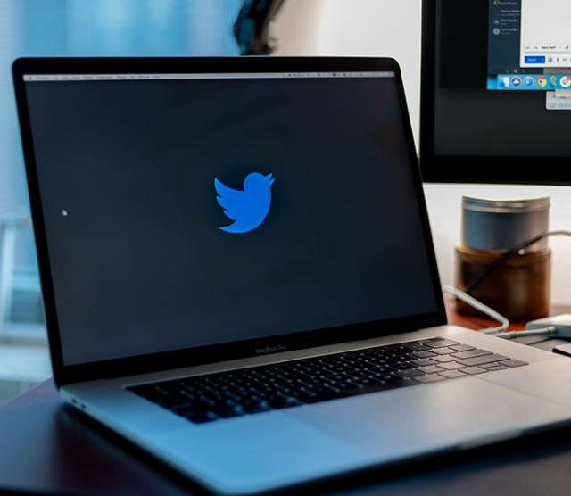 An image of laptop computer open with the Twitter icon displayed, and a projector screen in the background