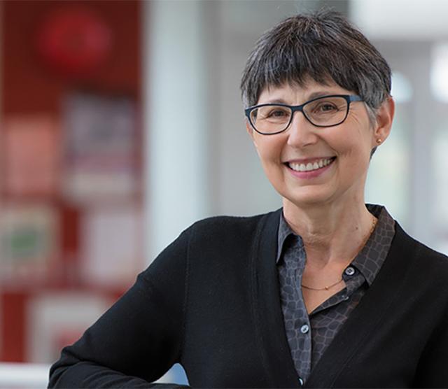 A headshot of Janet Werker, smiling, with one arm placed on a railing