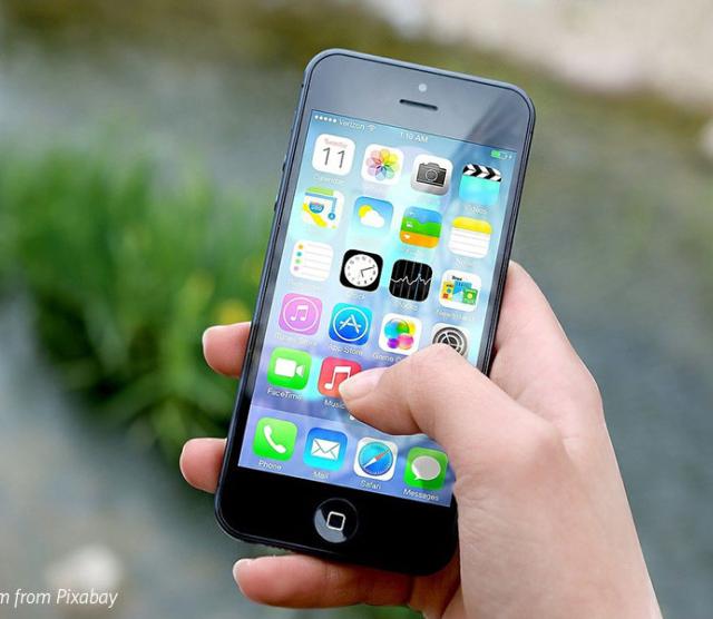 An image of a hand holding an iPhone above the ground, with apps showing on the screen