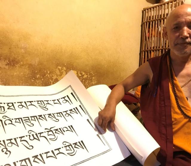A picture of a Tibetan monk holding a large scroll upon which Tibetan characters are written.