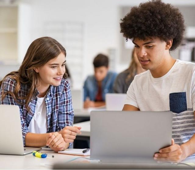 Two secondary school students working together on laptops.