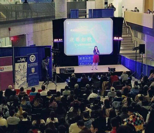 A picture of Zoe Lam onstage at a Cantonese languagae program event in a mall, in front of a crowd of people