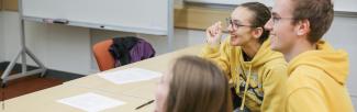 A picture of three students in the Living Language class, sitting at a table and laughing while they look towards the front of the class