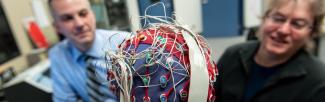 A picture of Drs Tony Herdman and Sid Fels looking at a cap covered in electrodes on a research assistant.
