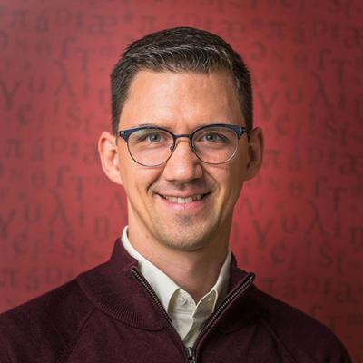 A headshot of Johannes Heim smiling and standing against a red background