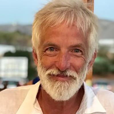 A headshot of Douglas Pulleyblank wearing a white shirt, standing in front of a cityscape.