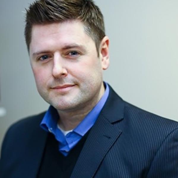 A headshot of Steven Aiken standing in front of a grey background