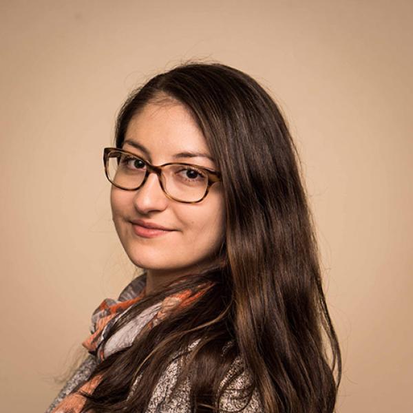 A headshot of Denitza Dramkin standing in front of a brown background