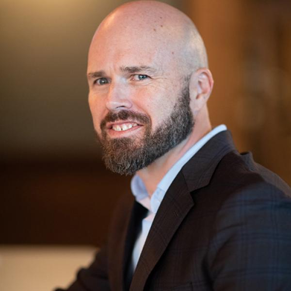 A headshot of Dr. Gramling looking over his shoulder into the camera, wearing a black jacket and blue shirt