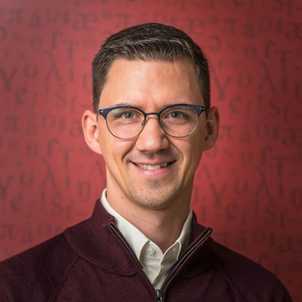 A headshot of Johannes Heim smiling and standing against a red background