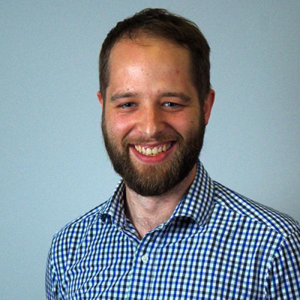 A headshot of Nick Peatfield standing in front of a blue background