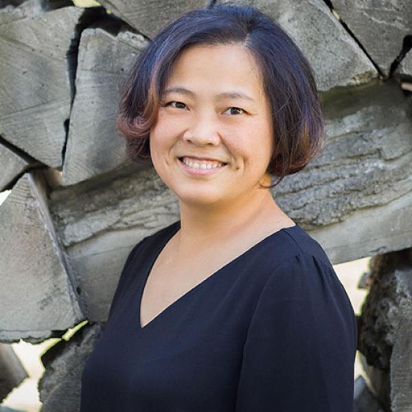 A picture of Qian Wang smiling and standing in front of a rock wall.