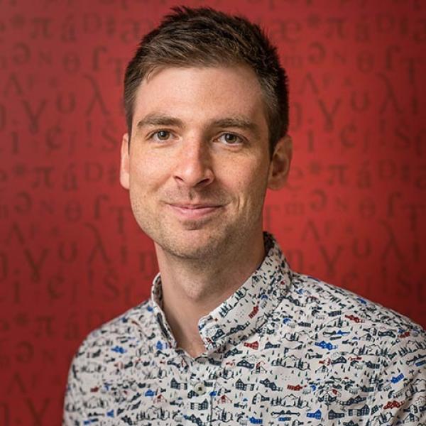 A headshot of Márton Sóskuthy standing in front of a red background