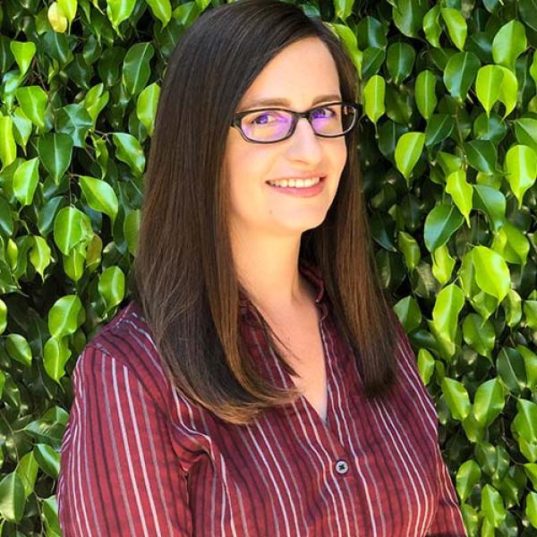 A headshot of Elise Stickles standing side on to the camera, in front of leaves